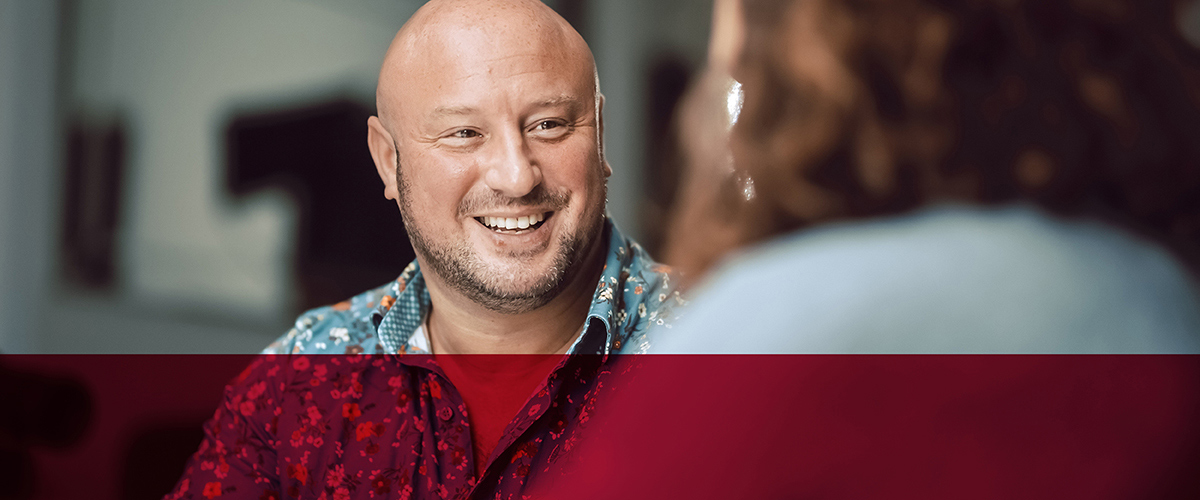 smiling-man-talking-to-blurry-figure-in-foreground-layth